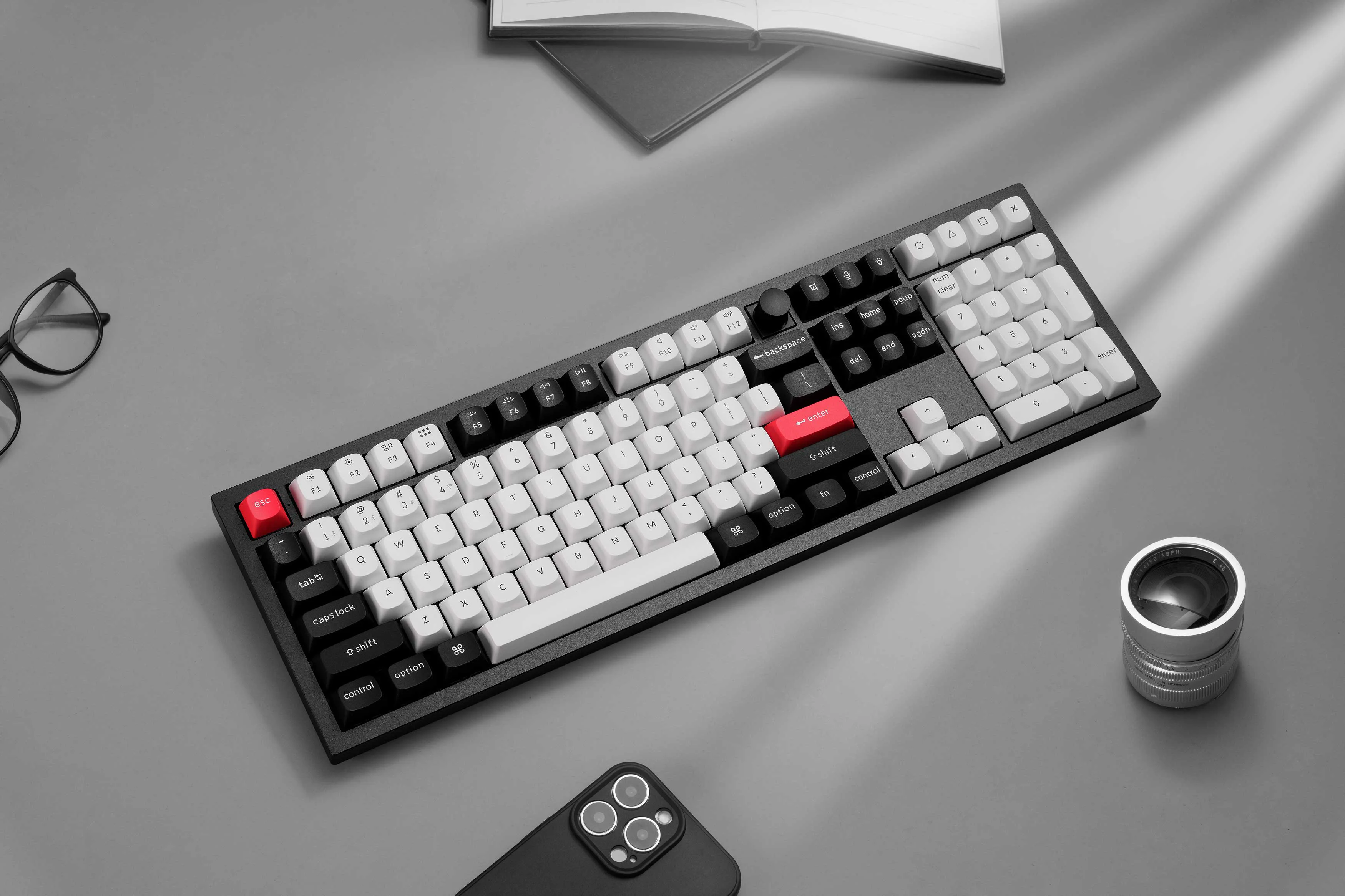 Clavier mécanique Keychron full-size avec touches noires et blanches et accents rouges sur un bureau avec lunettes et smartphone