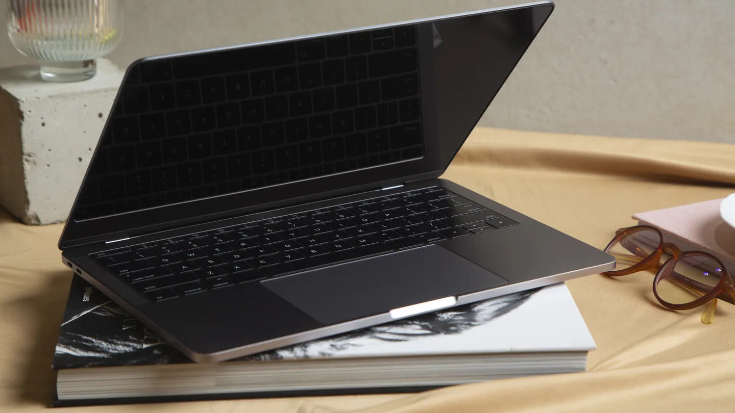 PC portable fin à l'écran éteint, ouvert sur une pile de livres à côté d'une paire de lunettes