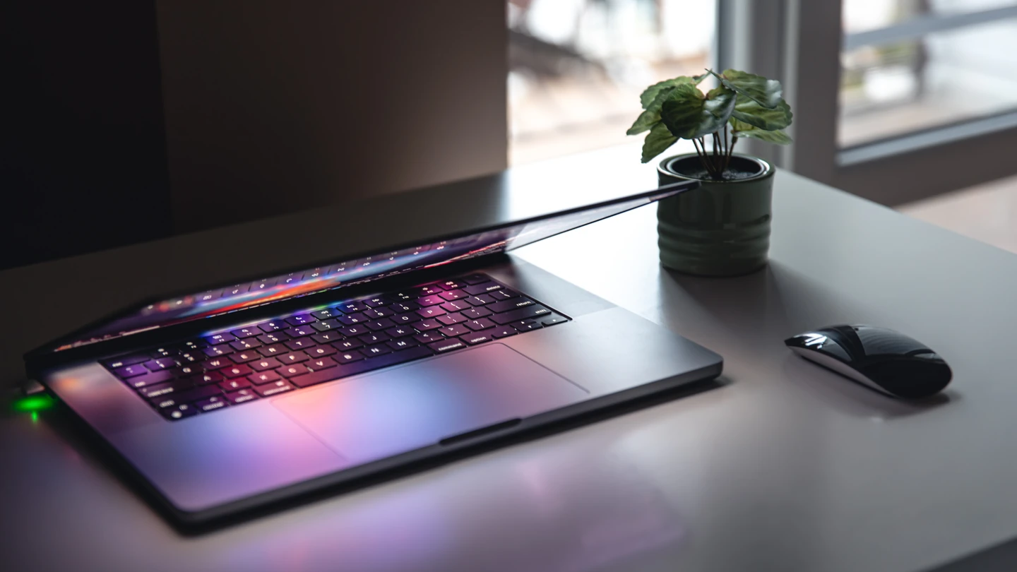 PC portable entrouvert au clavier rétroéclairé, sur un bureau à côté d'une plante et d'une souris
