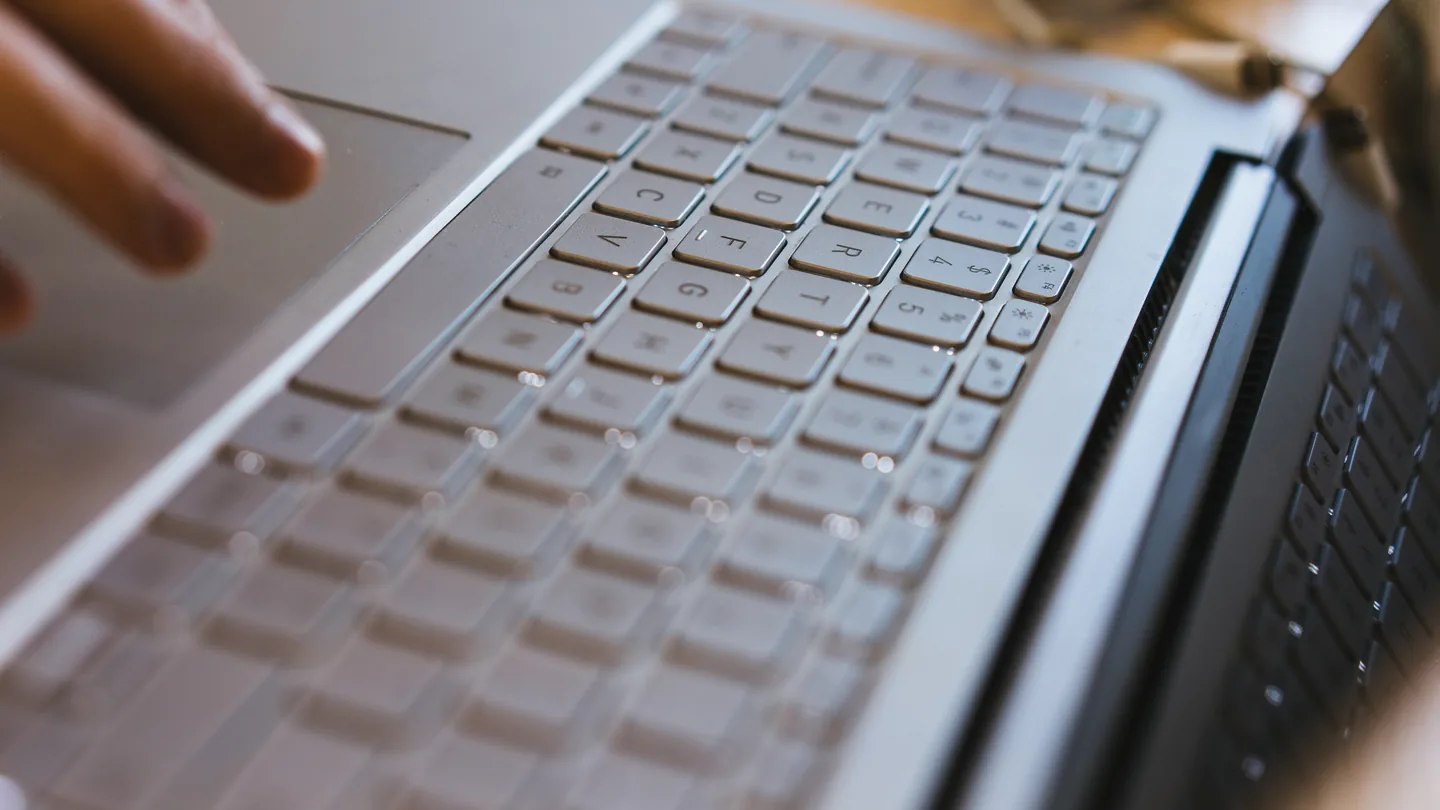 Gros plan sur un clavier de PC portable avec une main qui s'approche des touches