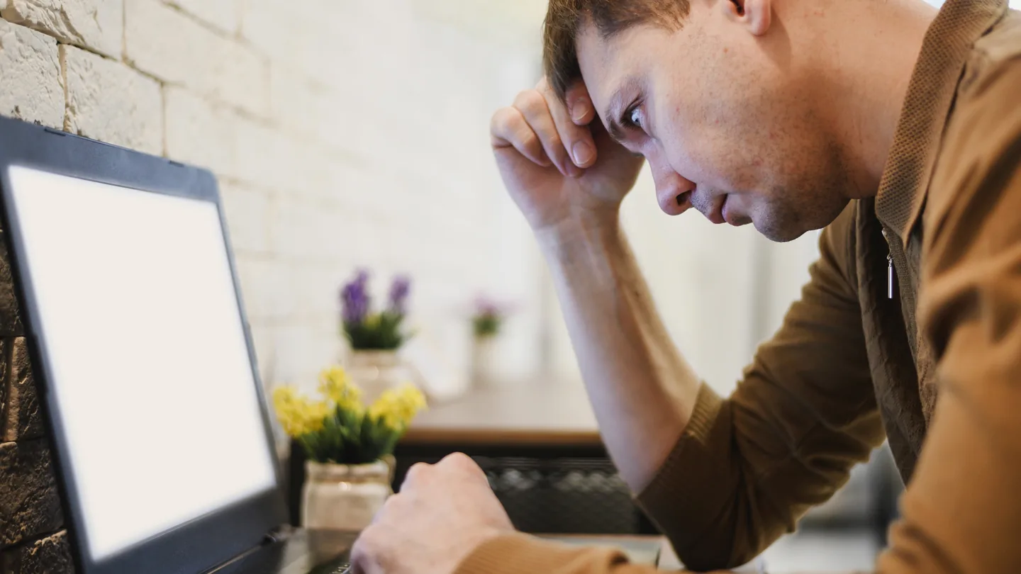 Un homme la tête dans la main devant un PC portable à l'écran vide
