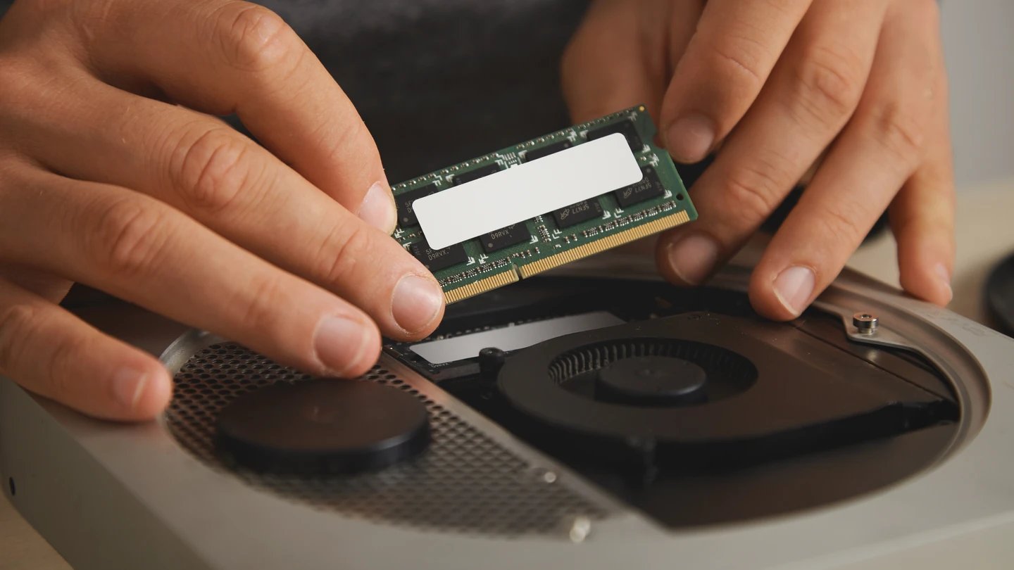 Deux mains installent une barrette de mémoire dans un PC portable ouvert